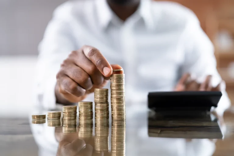 Person stacking coins, using calculator for budgeting.