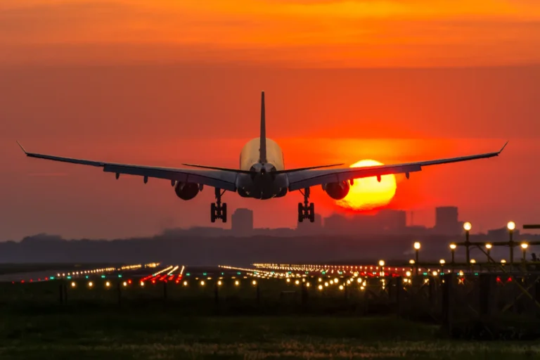 Airplane landing at sunset with runway lights on.