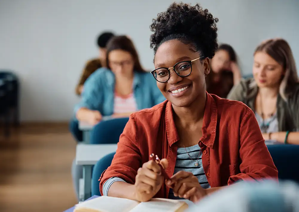 Student smiling in classroom with open book.