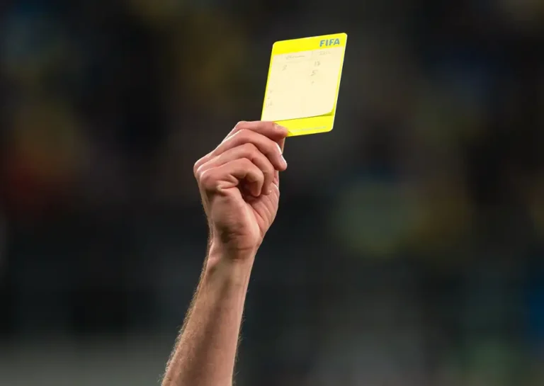 Referee holding a yellow card during soccer match.