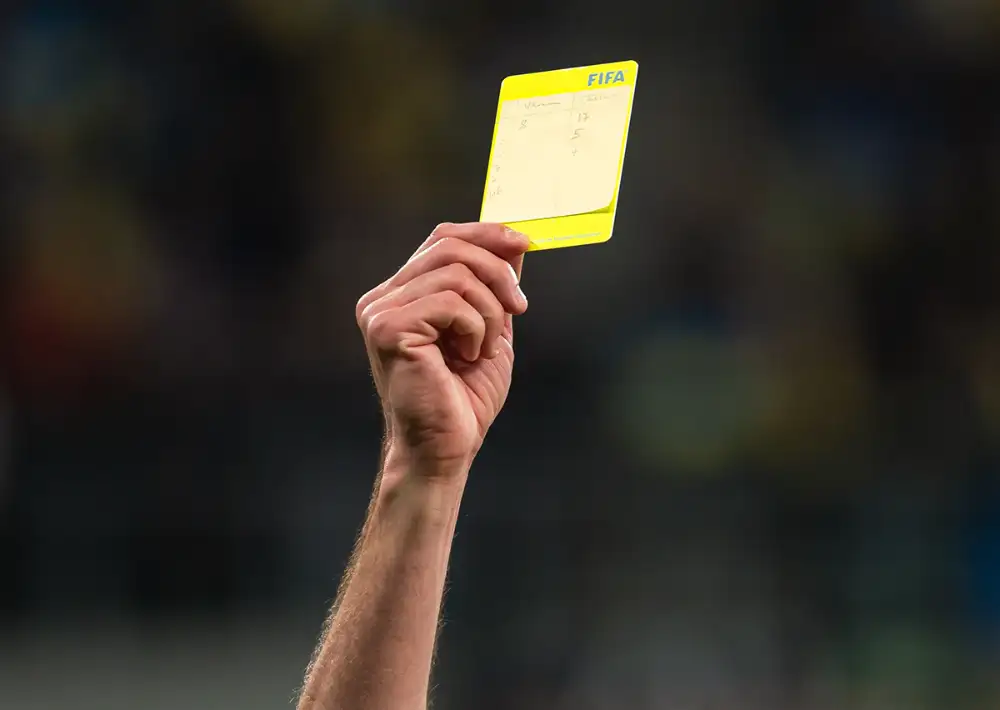 Referee holding a yellow card during soccer match.